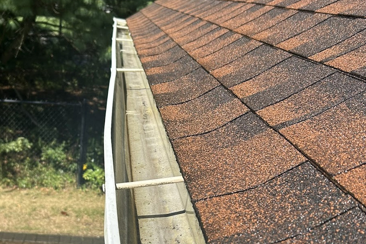 Detailed view of a clear gutter channel on a brown shingle roof for gutter cleaning in Long Island.